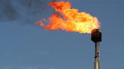 A gas tower spews flames against a blue sky.