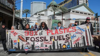 Protesters marching with a sign that reads, "99% of plastics is made from fossil fuels."