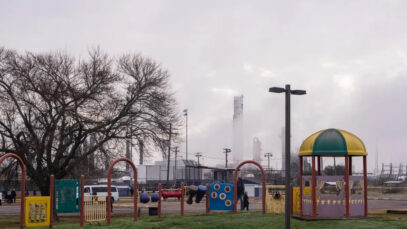 A children's playground with a smoky plastics factory in the background.